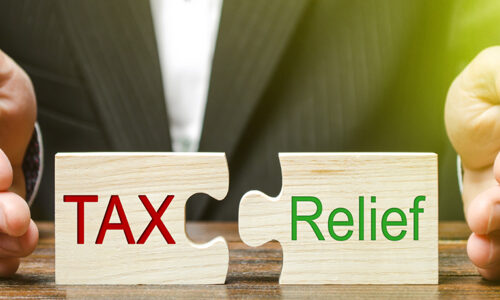 A businessman puts two puzzles with the words Tax and Relief. The concept of reducing the debt burden on business and local production to increase the competitiveness of their products. Economy